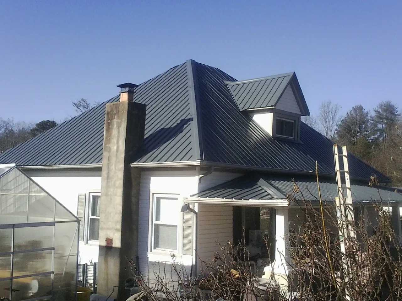 Dark blue standing seam metal roof on a white farmhouse with dormer — Slate & Tile Roof Repair by Roofing Brothers in Austinburg