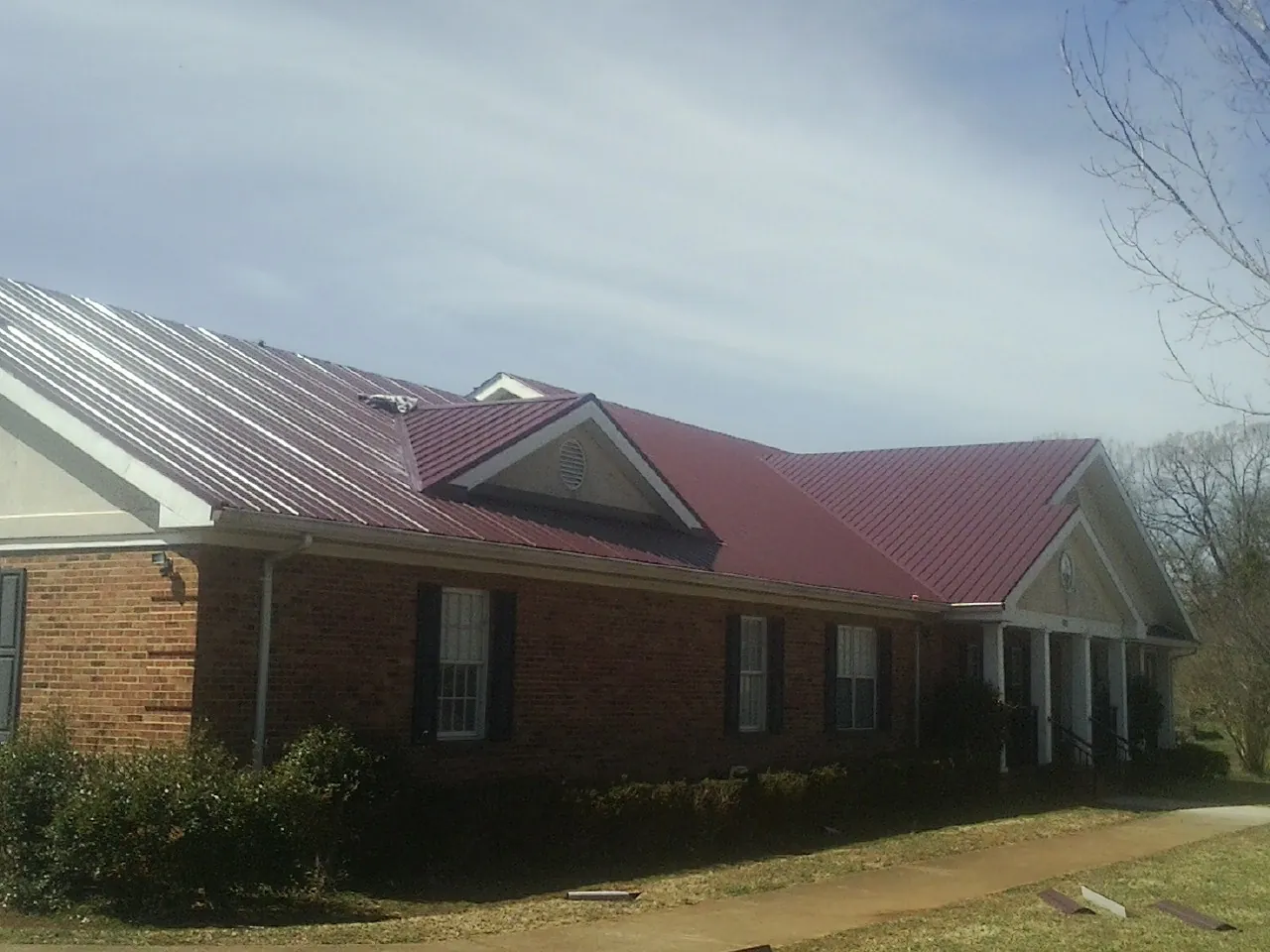 Red metal roof with gabled entries on a long brick building, from a Hail Damage Roof Repair job in Austinburg