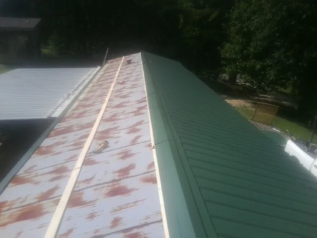 Old rusted panels beside newly installed green metal roofing — Wind Damage Roof Repair by Roofing Brothers in Austinburg
