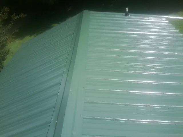 New green metal panels meeting at the ridge of a roof — Flat Roof Repair work by our crew in Austinburg