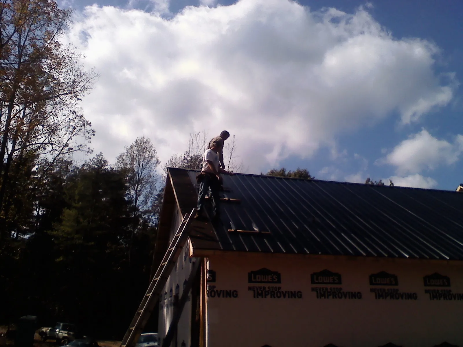 Roofer fastening dark metal panels high against a cloudy sky, from a Roof Inspection job in Austinburg