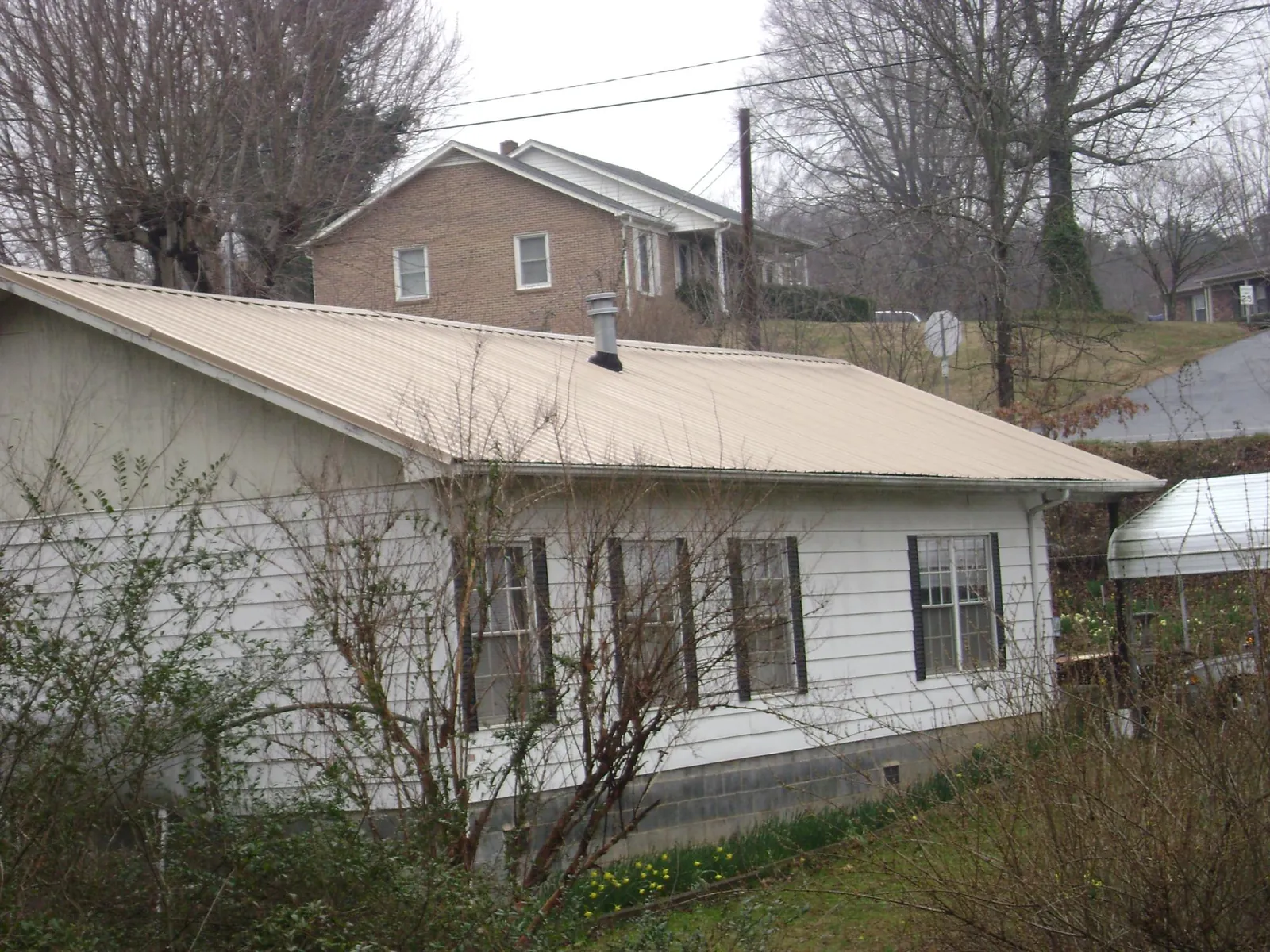 Tan metal roof on a white sided house set into a hillside — Commercial Roofing by Roofing Brothers in Austinburg