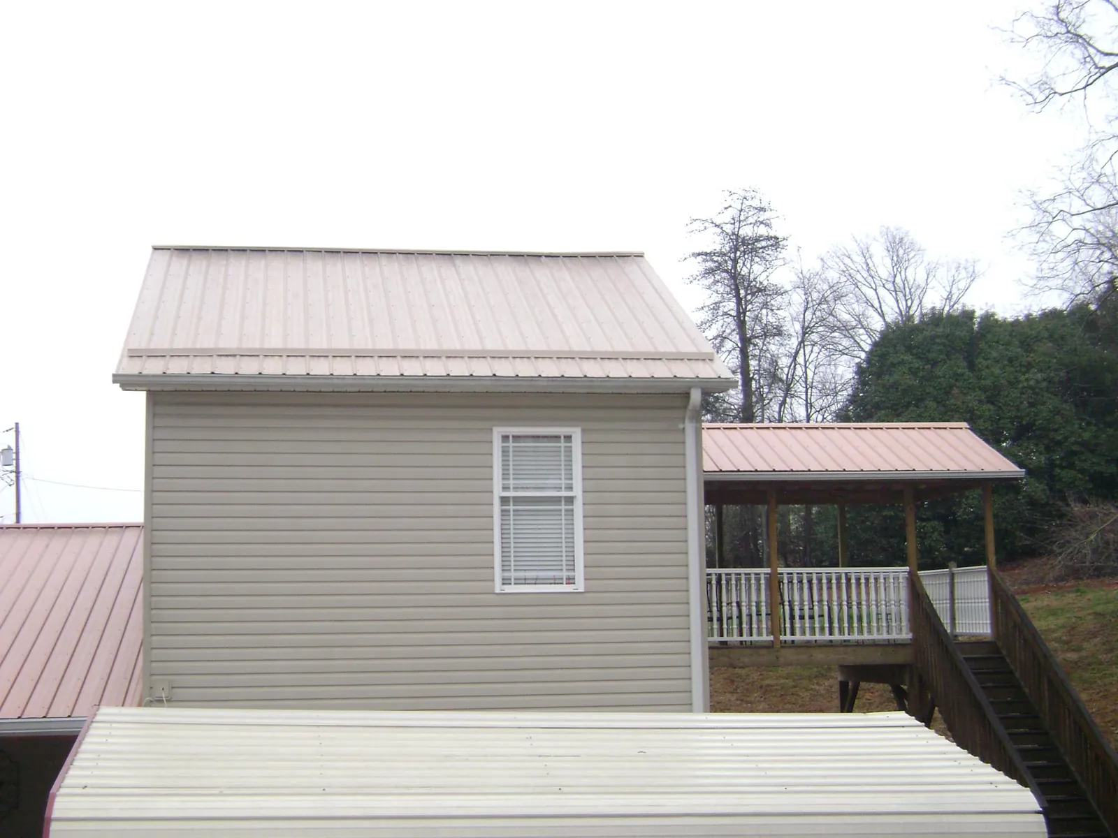 Tan metal roofs on a two story addition and attached porch, from a Roof Replacement job in Austinburg